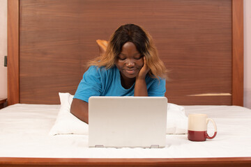 young african woman using her laptop in bed