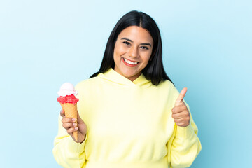 Young Colombian woman with a cornet ice cream isolated on blue background with thumbs up because something good has happened