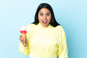 Young Colombian woman with a cornet ice cream isolated on blue background with surprise and shocked...