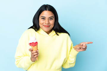 Young Colombian woman with a cornet ice cream isolated on blue background surprised and pointing...