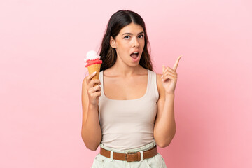 Young caucasian woman with a cornet ice cream isolated on pink background thinking an idea pointing...