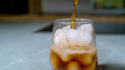 CLOSE UP: Soda gets poured over the ice cubes melting in the elegant glass.