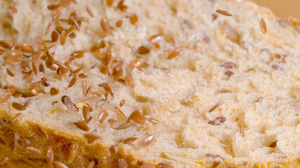 MACRO: Shiny red and brown flaxseeds fall on a rustic loaf of bread cut in half
