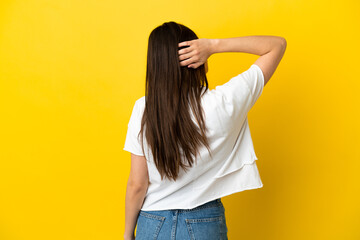 Young caucasian woman isolated on yellow background in back position and thinking