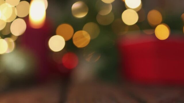 blurred and soft focus of red gift box ball decorations and Christmas fir tree branch with golden yellow garland blinking defocused lights on wooden background. holiday mood celebration concept