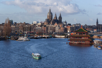 Passenger boat crosses the Amsterdam river against the backgound of historical church and famous floating Chinese restaurant, Netherlands. The beautiful winter weather.