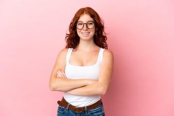 Teenager reddish woman isolated on pink background keeping the arms crossed in frontal position