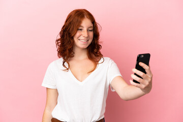Teenager reddish woman isolated on pink background making a selfie with mobile phone
