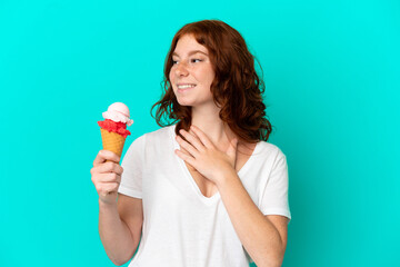 Teenager reddish woman with a cornet ice cream isolated on blue background looking up while smiling