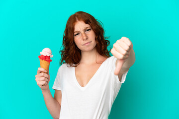 Teenager reddish woman with a cornet ice cream isolated on blue background showing thumb down with negative expression
