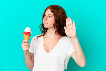 Teenager reddish woman with a cornet ice cream isolated on blue background making stop gesture and disappointed