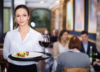 Professional happy cheerful positive waitress holding serving tray for restaurant guests