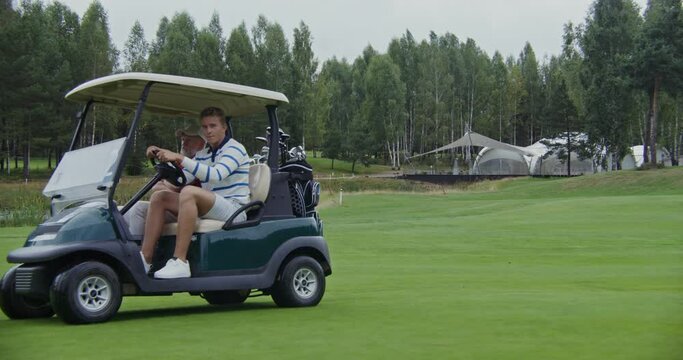 Two men are driving a golf car on a golf course and talking to each other
