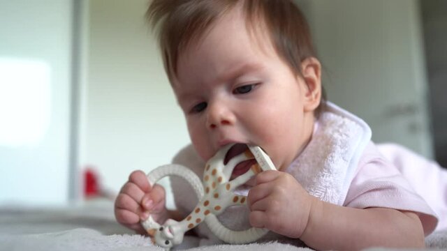Small caucasian baby four or five months old having teeth growing issues teething pain while holding a bite toy looking to the camera lying on the bed with teether at home
