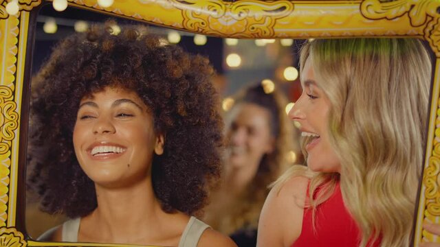 Female friends having fun posing with photo booth photo frame at party in bar - shot in slow motion