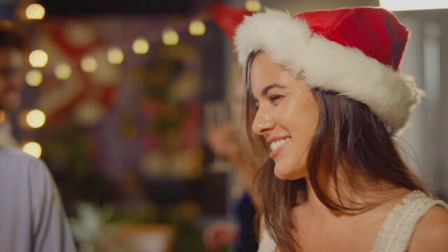 Multi-cultural group of friends wearing santa hats celebrating  enjoying Christmas party night out in bar or club - shot in slow motion