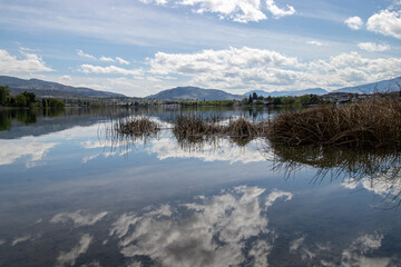 clouds reflecting in a calm lake surrounded by mountains at Tuguinuit Lake in Oliver, British...