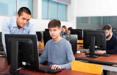 Fototapeta na wymiar Male trainer helping young female student in computer class. High quality photo