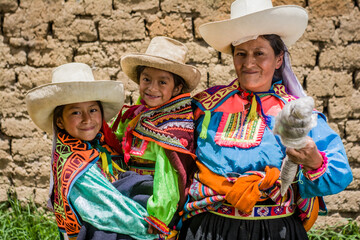 Mujer madre latinoamericana andina haciendo hilo de lana de oveja y enseñando el telar de cintura a sus hijas.