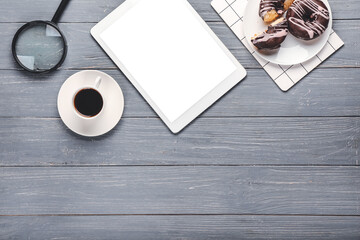 Cup of coffee, tablet computer, magnifying glass and donuts on wooden background