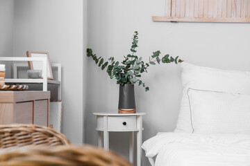 Black vase with eucalyptus on nightstand in light bedroom