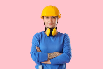 Female construction worker with hardhat and ear protectors on pink background