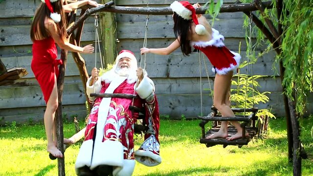Funny crazy santa swinging with sexy santa girls snow maiden. Christmas party concept. Santa senior man with sexy woman.