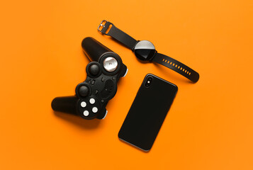Modern joystick, smart watch and mobile phone on orange background
