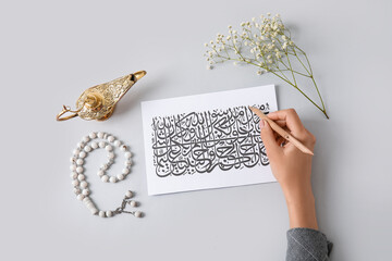 Arabic calligraphist writing on paper sheet against light background