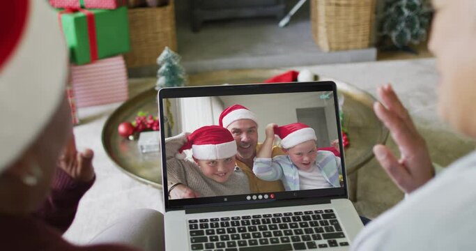 Two diverse senior female friends using laptop for christmas video call with family on screen
