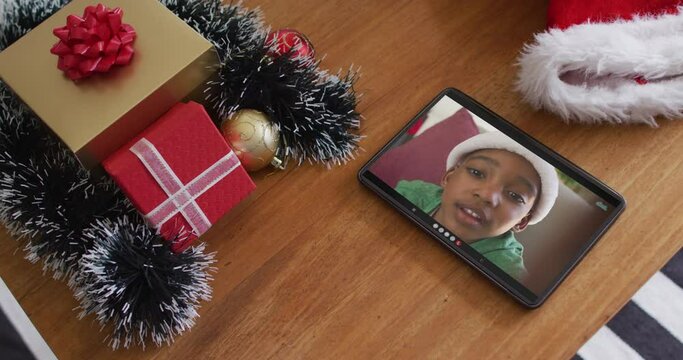 Smiling african american boy wearing santa hat on christmas video call on tablet