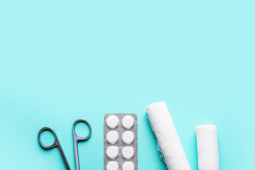Surgical scissors, pills and medical bandage rolls on color background, closeup