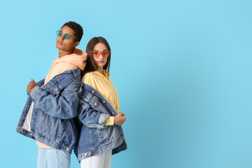 Fototapeta premium Stylish young couple in hoodies and denim jackets on blue background