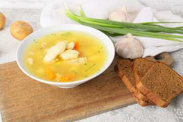 Wooden board with bowl of delicious dumpling soup and bread on light background