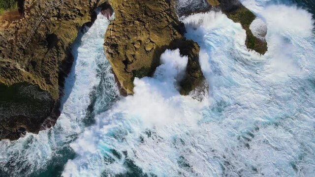 Big ocean waves crashing on the rocks of Devil's Tear at Nusa Lembongan Bali Indonesia. Drone top-down view.