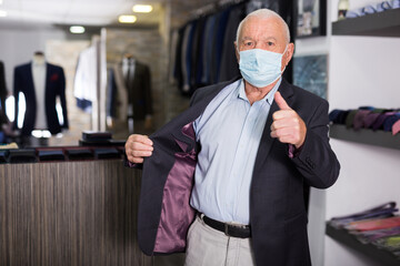 Fototapeta na wymiar Senior customer in protective mask trying on a fashion jacket in the men's boutique