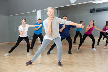 Fototapeta na wymiar Portrait of sporty smiling mature woman practicing vigorous lindy hop movements in dance class