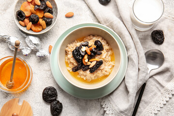 Composition with delicious oatmeal, prunes and almond nuts in bowl on light table