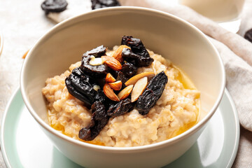 Bowl with delicious oatmeal, prunes and almond nuts on table, closeup