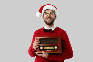 Young man with Christmas decor and retro radio receiver on grey background