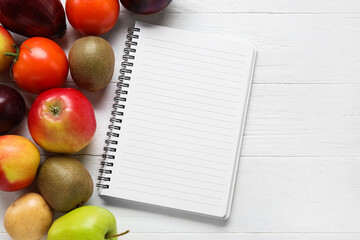 Blank notebook, vegetables and fruits on light wooden background. Vegan Day, closeup