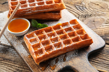 Board with delicious Belgian waffles and honey on wooden background, closeup