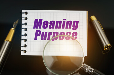 On the black surface is a pen, a magnifying glass and a notebook with the inscription - Meaning...