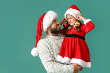 Little girl and her father in Santa hats on color background