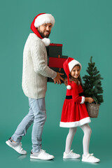 Little girl and her father with Christmas tree and gifts on color background
