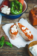 Wholegrain bread covered with tomato-pepper dip and feta cheese over old rustic wooden table. Homemade organic vegetable dish.