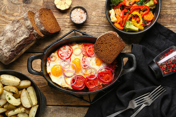 Baking dish with tasty Shakshouka, vegetables and fried potatoes on wooden background