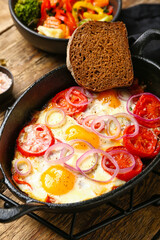 Baking dish with tasty Shakshouka on wooden background