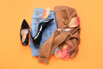 Stylish clothes, accessories and dry leaves on color background