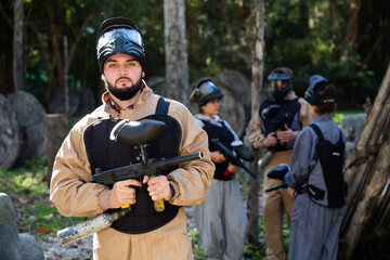 Man and his paintball sport team in protective uniform at paintball shooting range